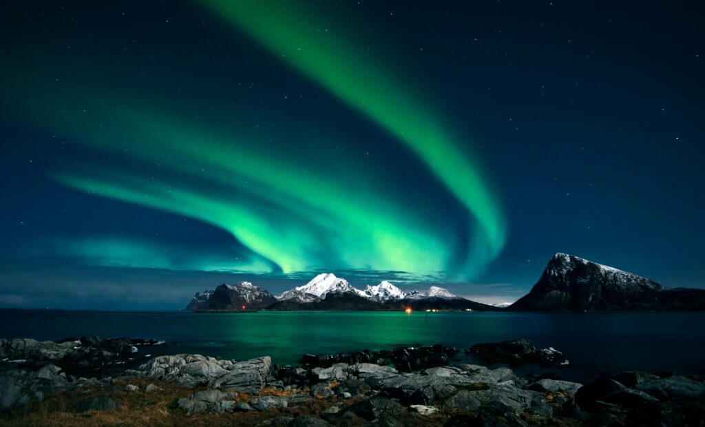 Breathtaking northern lights display over snow-covered mountains and serene waters in Lofoten, Norway.